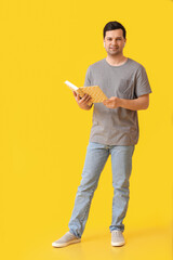 Wall Mural - Young man with book and earphones on color background