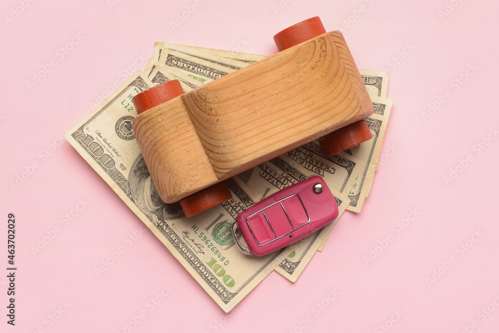 Wooden car with key and banknotes on pink background