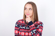 © Roquillo - Thoughtful Young caucasian girl wearing christmas sweaters on white background holds chin and looks away pensively makes up great plan