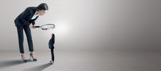 Canvas Print - Female in suit using magnifier magnifying glass to look at tiny subordinate on concrete background with shadow and mock up place. Hiring and dominance concept.