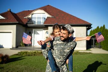 Portrait of father soldier in uniform on military leave holding his lovely daughter in front of their house.
