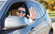 © Julija - Cheerful young man saying hello, waving his hand while he drives his new car.