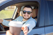 © Julija - young smiling man driving car and taking away coffee.