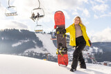 Young woman with snowboard on the slope of hill at winter resort