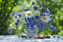 Bright Cheerful Still Life With Fresh Daisies And Beautiful Cornflowers In A White Pot With A Blue Pattern On A Green Blurred Background Of A Summer Sunny Garden