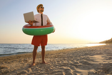 Canvas Print - Happy man with inflatable ring and laptop on beach, space for text. Business trip