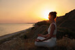 © New Africa - Mature woman meditating on hill near sea at sunset. Space for text