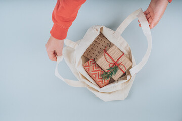 Child takes out of the fabric trend bag organic Christmas Presents decorated spruce twigs on a gray background. Flat lay, top view. High quality photo