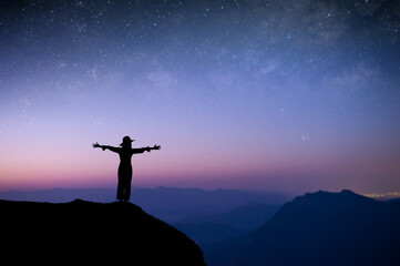 Wall Mural - Silhouette of young female standing with both hands above your head watched the star and milky way alone on top of the mountain. She enjoyed traveling and was successful when he reached the summit.