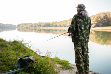 Wall Mural - senior concept. A fisherman on river catches predatory fish. Useful hobby, beautiful autumn, active healthy lifestyle. rear view