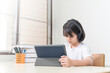 © EduLife Photos - Cheerful Asian little girl student wears headphone, writes on digital tablet to study at home. Education Concept Stock Photo
