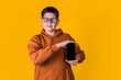 © Valeriia - handsome boy with glasses in a brown sweatshirt holding a phone  on a yellow background