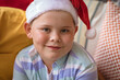 © wavebreak3 - Portrait of caucasian boy wearing santa hat sitting on the couch at home during christmas