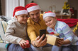 © wavebreak3 - Caucasian father and two sons opening gift box during video call on smartphone during christmas