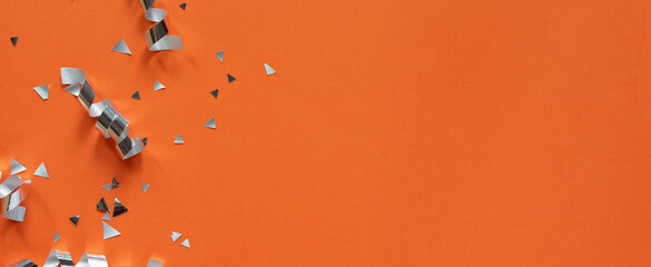 Wall Mural - close up on group of silver color of rolling ribbon and confetti on panoramic orange background with