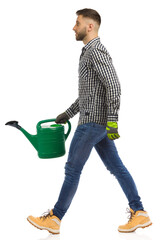 Wall Mural - Young man is walking with green watering can. Side view. Studio shot, isolated.