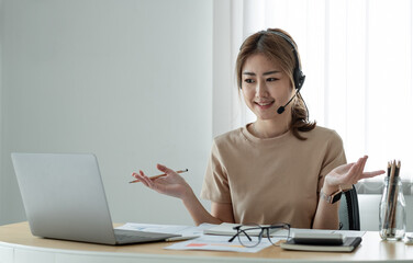 Smiling asian woman freelancer wearing headset, communicating with client via video computer call. Millennial pleasant professional female tutor giving online language class