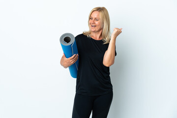 Wall Mural - Middle age woman going to yoga classes while holding a mat isolated on white background celebrating a victory