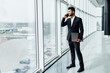 © Тарас Нагирняк - An attractive Indian man in a black suit, with a computer in his hand talking on the phone, he is in a modern building, a company manager