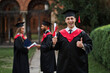 © Тарас Нагирняк - Happy caucasian graduate with his classmates in graduation gown holds diploma in campus