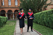 © Тарас Нагирняк - Two international graduate friends walking in university campus in graduation robes