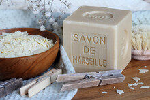 Marseille Soap Bar Named Savon De Marseille In French And Grated Soap On The Cotton Towel With Clothes Pegs And Washing Brush At Home Laundry Close Up. 