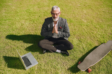 Wall Mural - A gray-haired businessman sitting on the grass and meditating