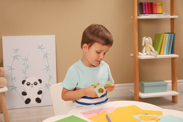 Poster - Little boy cutting color paper with scissors at table indoors