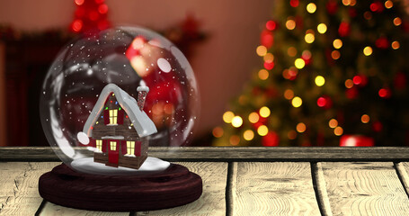 Image of snow globe with house on wooden table over christmas tree