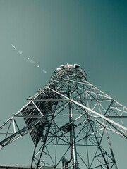 A Radio Tower on a mountain Top. The tower sits on top of the mountain against a blue sky surrounded by rocks and pine trees.