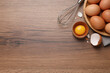 Chicken eggs, bowl with raw yolk and whisk on wooden table, flat lay. Space for text