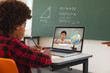 African american boy using laptop for video call, with biracial elementary school pupil on screen