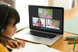 Asian girl using laptop for video call, with smiling diverse elementary school pupils on screen