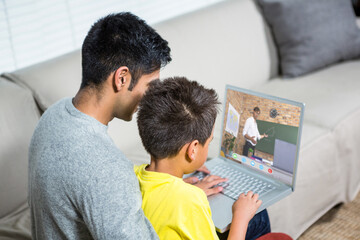 Wall Mural - Biracial boy with father using laptop for video call, with male teacher on screen