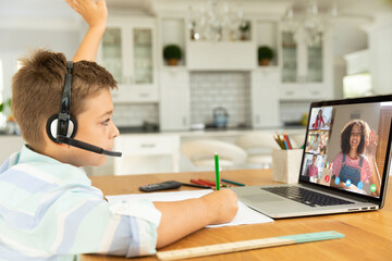 Canvas Print - Caucasian boy raising hand for video call, with waving diverse high school pupils on screen