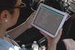 Biracial female programmer sitting in car, holding tablet with coding on screen