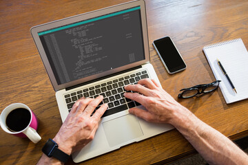 hands of caucasian male programmer siting at desk, using laptop with coding on screen