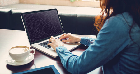 Midsection of caucasian female programmer sitting at desk and using laptop with coding on screen