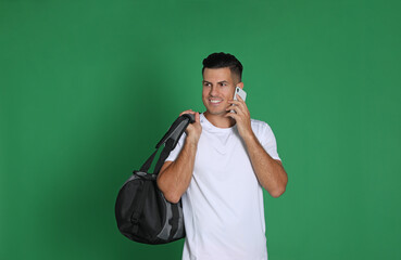 Wall Mural - Handsome man with sports bag and smartphone on green background