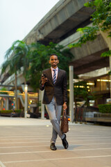 Wall Mural - Full length portrait of handsome young African businessman outdoors in city