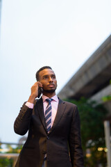 Wall Mural - Young African businessman outdoors in city talking on mobile phone