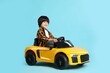 © New Africa - Little child driving yellow toy car on light blue background