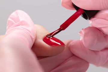 Wall Mural - Close up process of applying red varnish. Woman in salon receiving manicure by nail beautician. Red Nail polish and brush, macro. Shallow depth of field