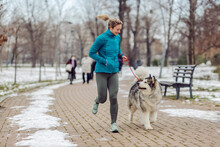 Sportswoman Jogging Together With Her Dog In Park On Snowy Weather. Winter Fitness, Pets, Friendship