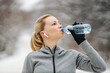 Sportswoman taking a break and drinking water while standing in nature at snowy winter day. Healthy habits, winter fitness, exercises