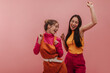 © Look! - Studio portrait of young asian and european woman happily singing and dancing in pink studio. Slim brunette and blonde with closed eyes in autumn casual clothes are having fun.