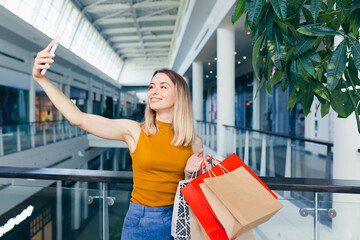 Wall Mural - young happy after shopping woman talking on cell in mall. Satisfied joyful female shopaholic with gift colored paper bags in hands. Mobile phone conversation. Smiling joy Stand ang sincerely tells