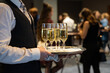 A waiter is holding a plate with sparkling wine to welcome people at an event. Glasses with champagne to toast. Drinks at a luxury party in a hotel.