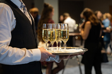 a waiter is holding a plate with sparkling wine to welcome people at an event. glasses with champagn