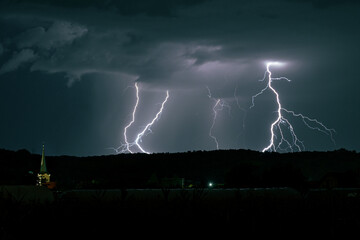Wall Mural - lightning bolts strike simultaneously behind a hill in the romanian landscape at night